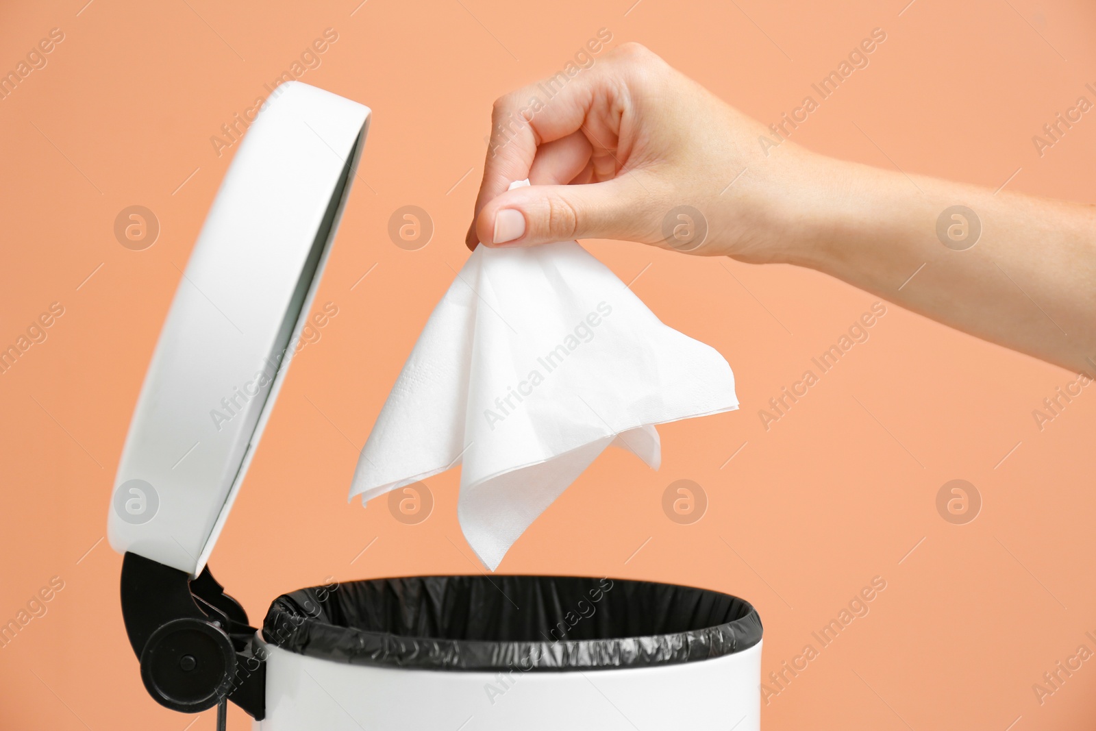 Photo of Woman putting paper tissue into trash bin on light brown background, closeup