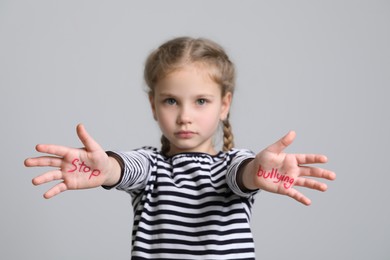 Girl showing hands with phrase Stop Bullying on light grey background, selective focus
