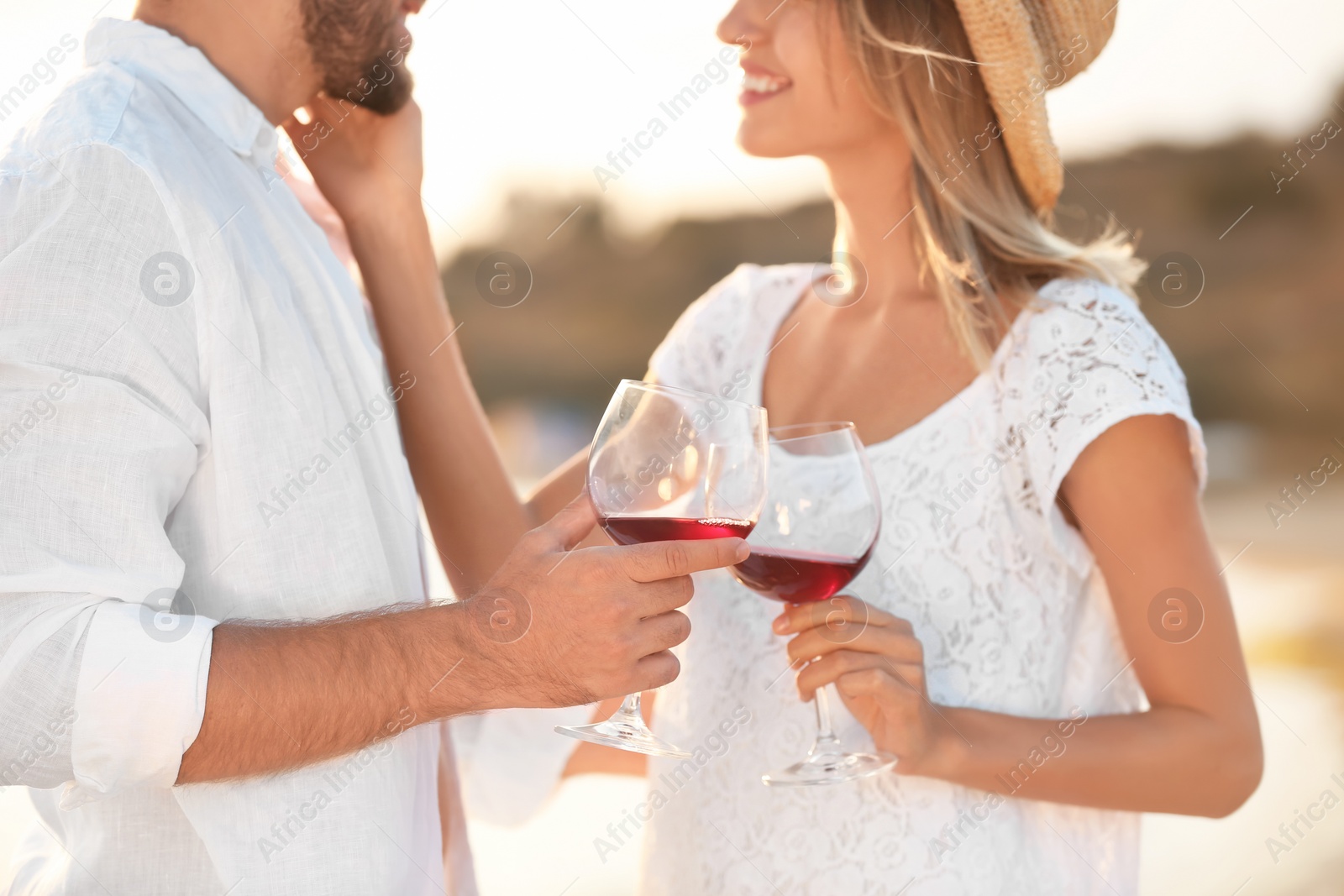 Photo of Young couple with glasses of wine on beach, focus on hands