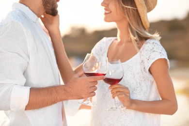 Photo of Young couple with glasses of wine on beach, focus on hands