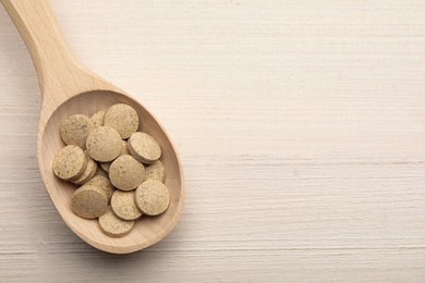 Spoon with dietary supplement pills on white wooden table, top view. Space for text