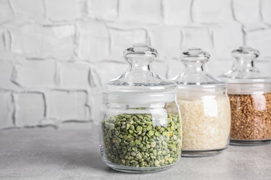 Photo of Dry peas and groats in jars on light grey table. Space for text