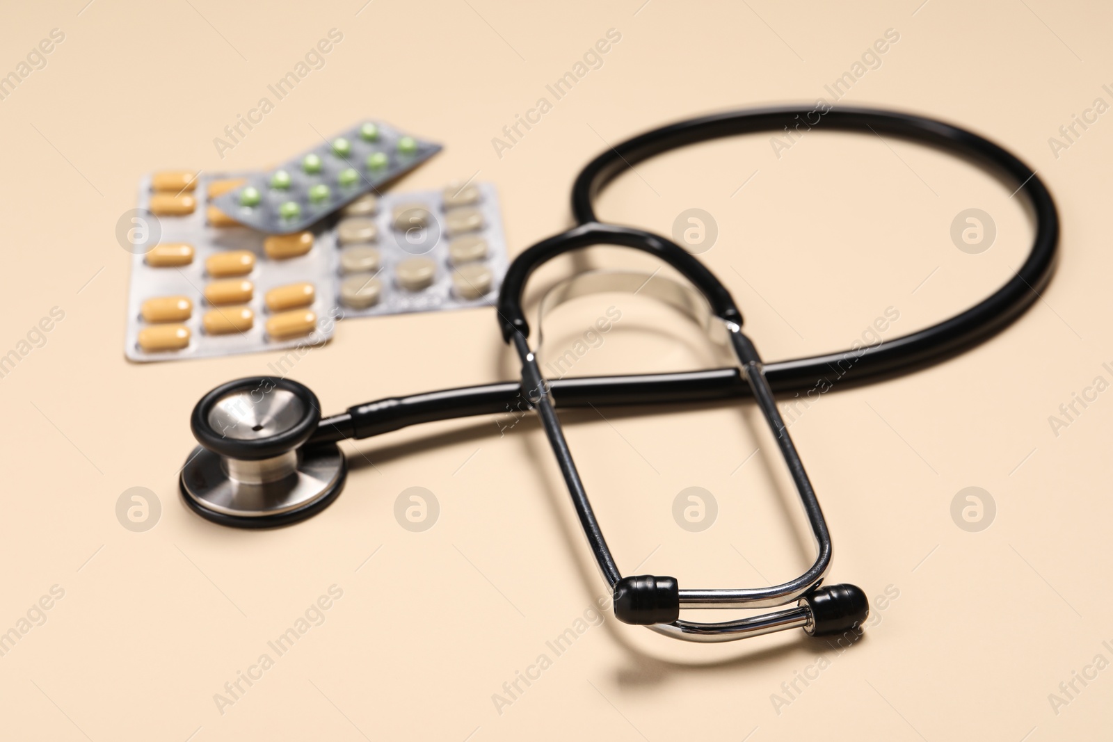 Photo of Stethoscope and pills on beige background, closeup. Medical tool