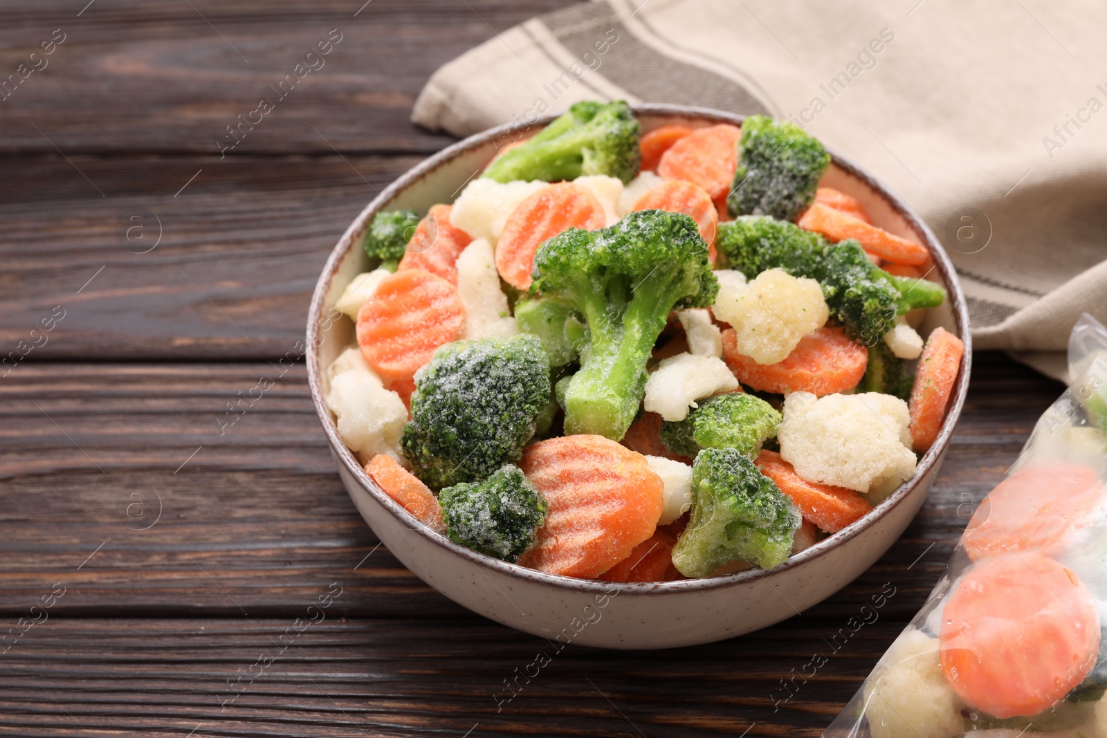 Photo of Mix of different frozen vegetables in bowl on wooden table, closeup. Space for text