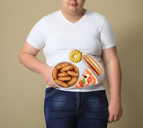 Image of Overweight man in tight t-shirt with images of different unhealthy food on his belly against beige background, closeup