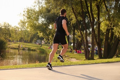 Photo of Man running near pond in park, back view