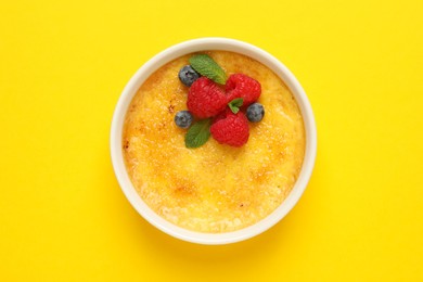Photo of Delicious creme brulee with fresh berries and mint on yellow background, top view