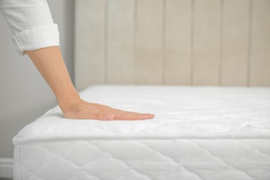 Woman touching soft white mattress indoors, closeup. Space for text