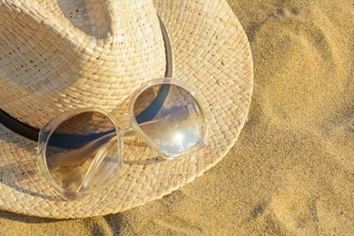 Hat with beautiful sunglasses on sandy beach, closeup