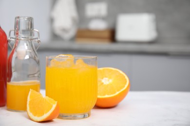 Photo of Tasty kombucha in glass, bottle and fresh orange on white table, space for text