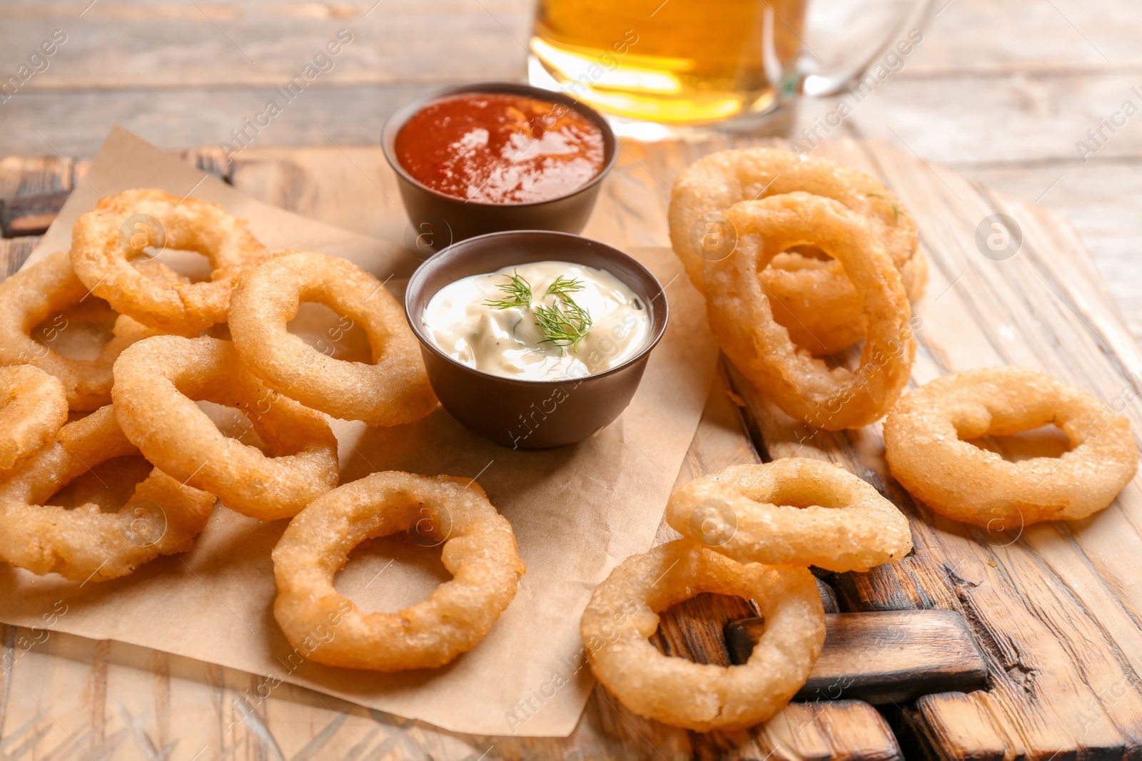 Photo of Fried onion rings served with sauces on wooden board, closeup