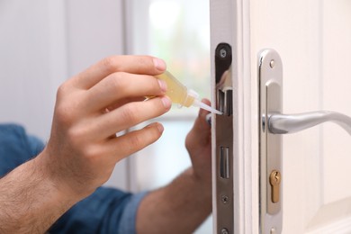 Photo of Repairman lubricating door lock at home, closeup