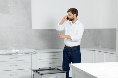 Man talking on smartphone in empty kitchen, space for text