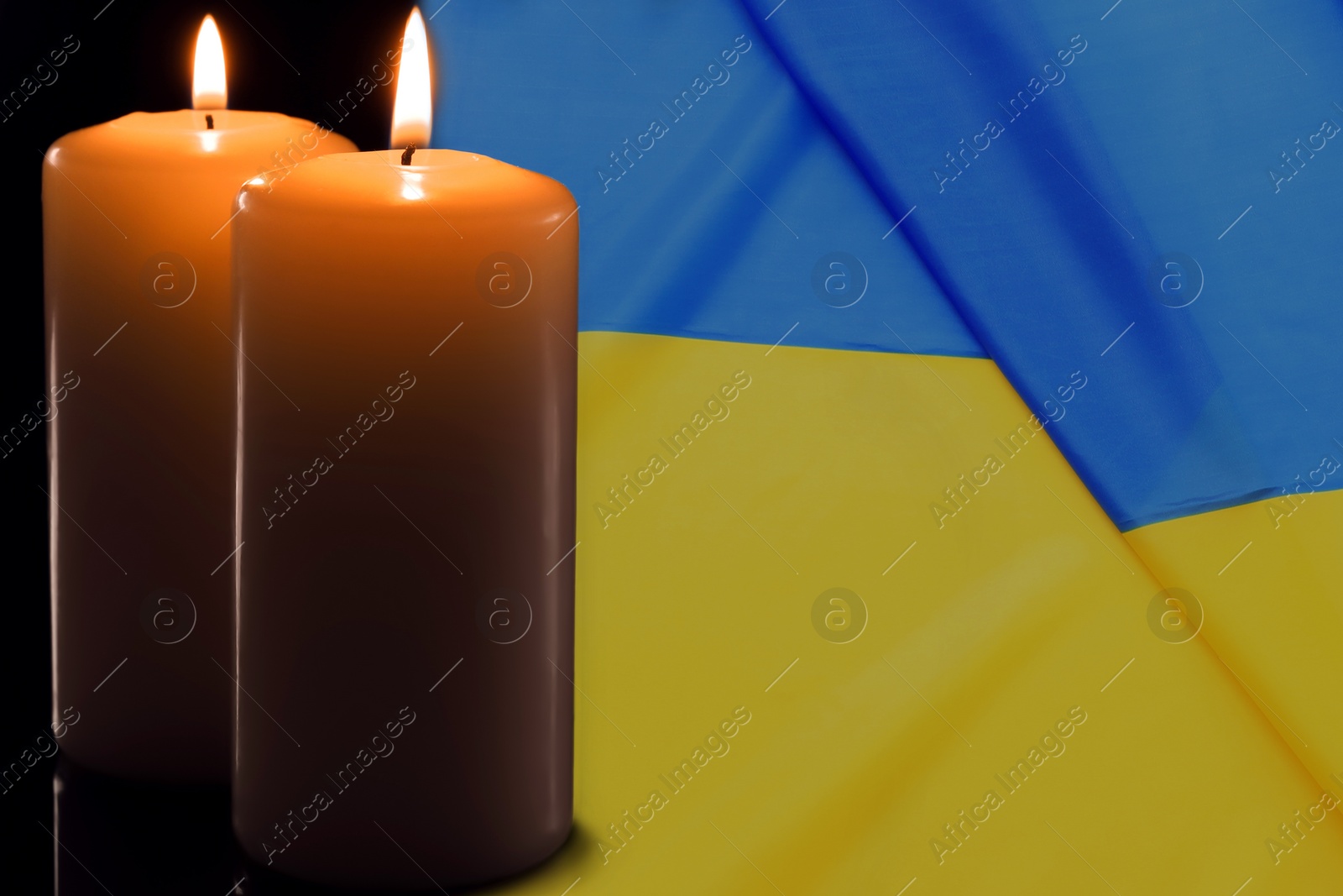 Image of Two burning candles and Ukrainian national flag on black background, closeup view. Space for text