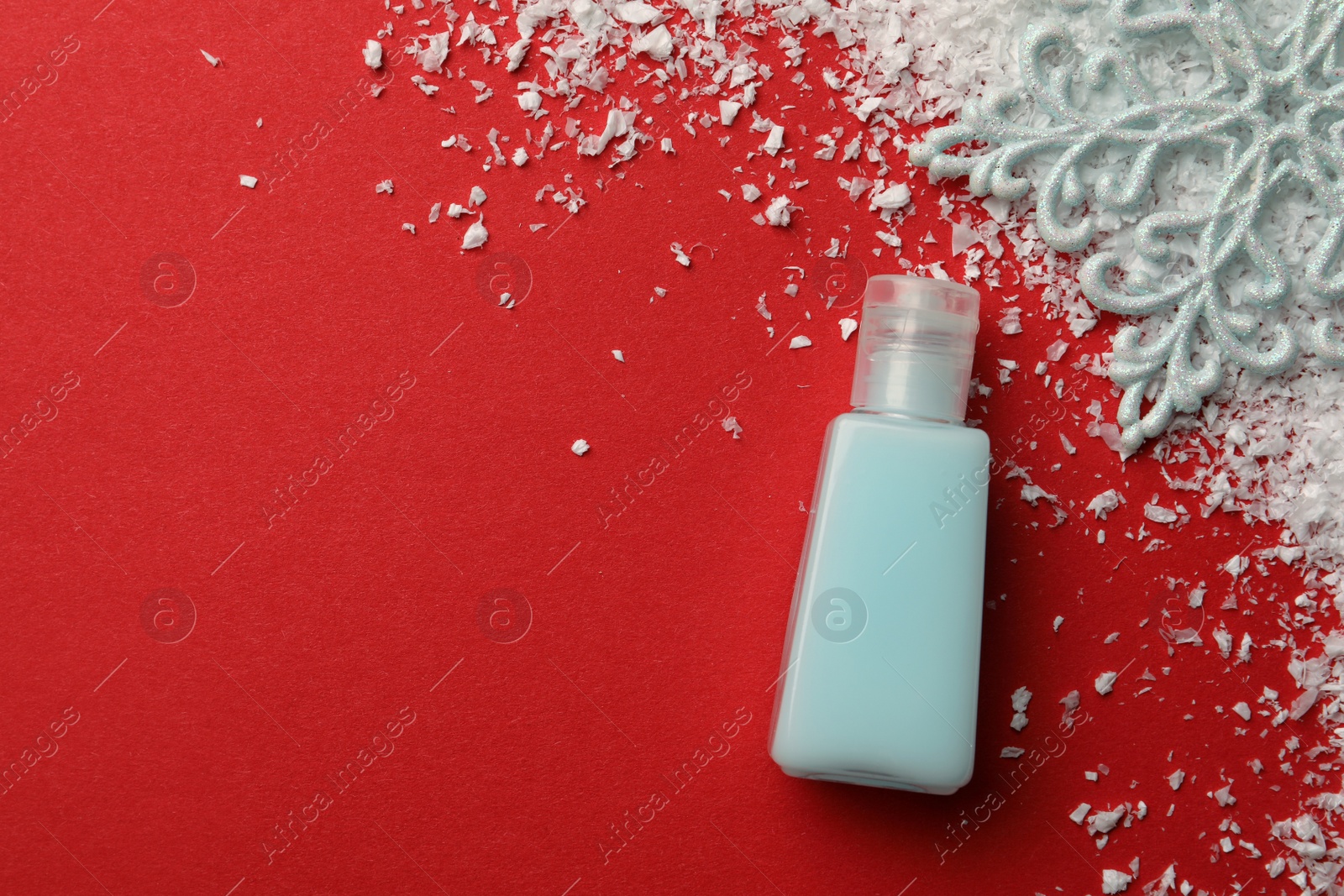 Photo of Winter skin care. Hand cream and artificial snow on red background, flat lay. Space for text