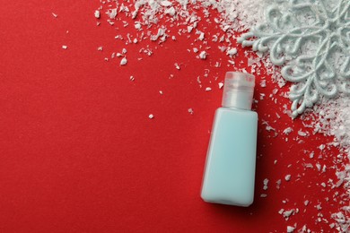 Winter skin care. Hand cream and artificial snow on red background, flat lay. Space for text