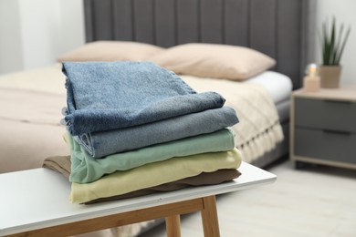 Photo of Stack of different folded clothes on bedside bench indoors, closeup