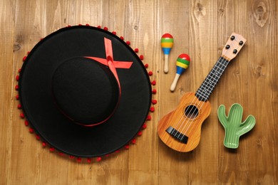 Photo of Mexican sombrero hat, maracas, toy cactus and guitar on wooden background, flat lay