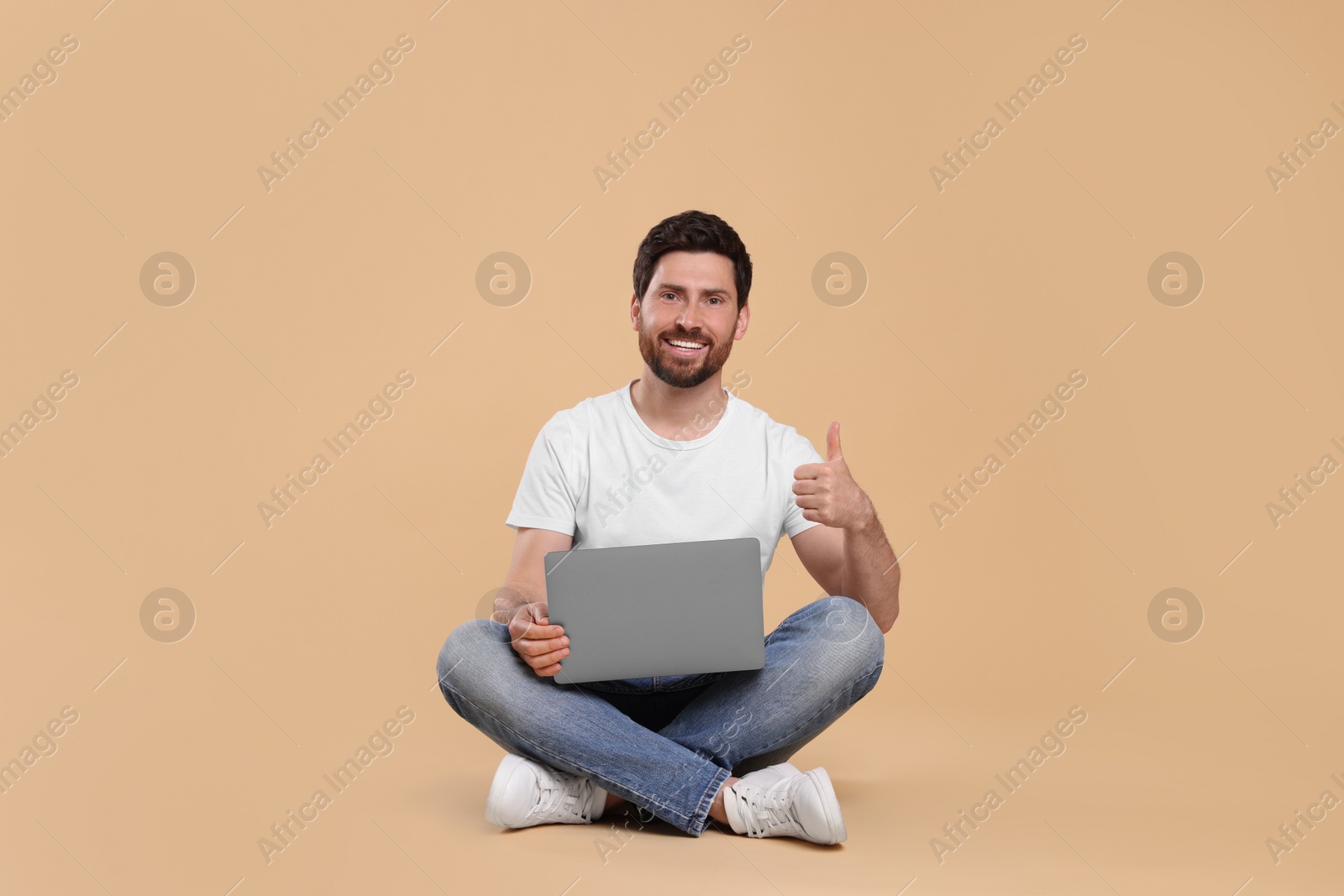 Photo of Happy man with laptop showing thumb up on beige background