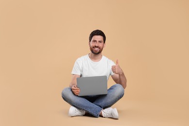 Photo of Happy man with laptop showing thumb up on beige background