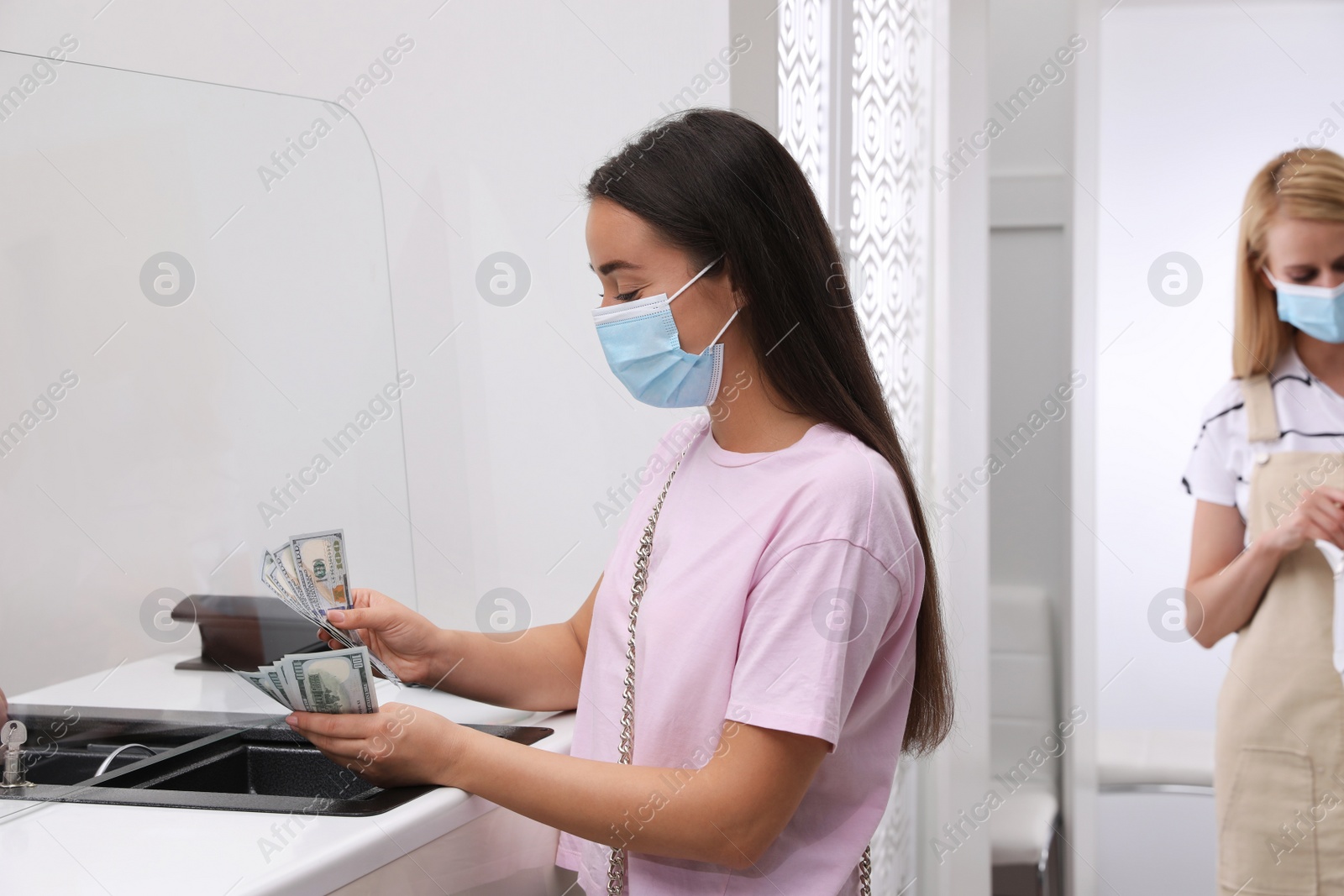 Photo of Woman with protective mask counting money at cash department window in bank. Currency exchange