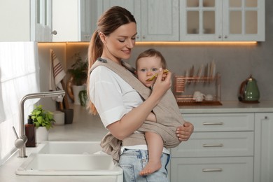 Mother feeding her cute child in sling (baby carrier) at home