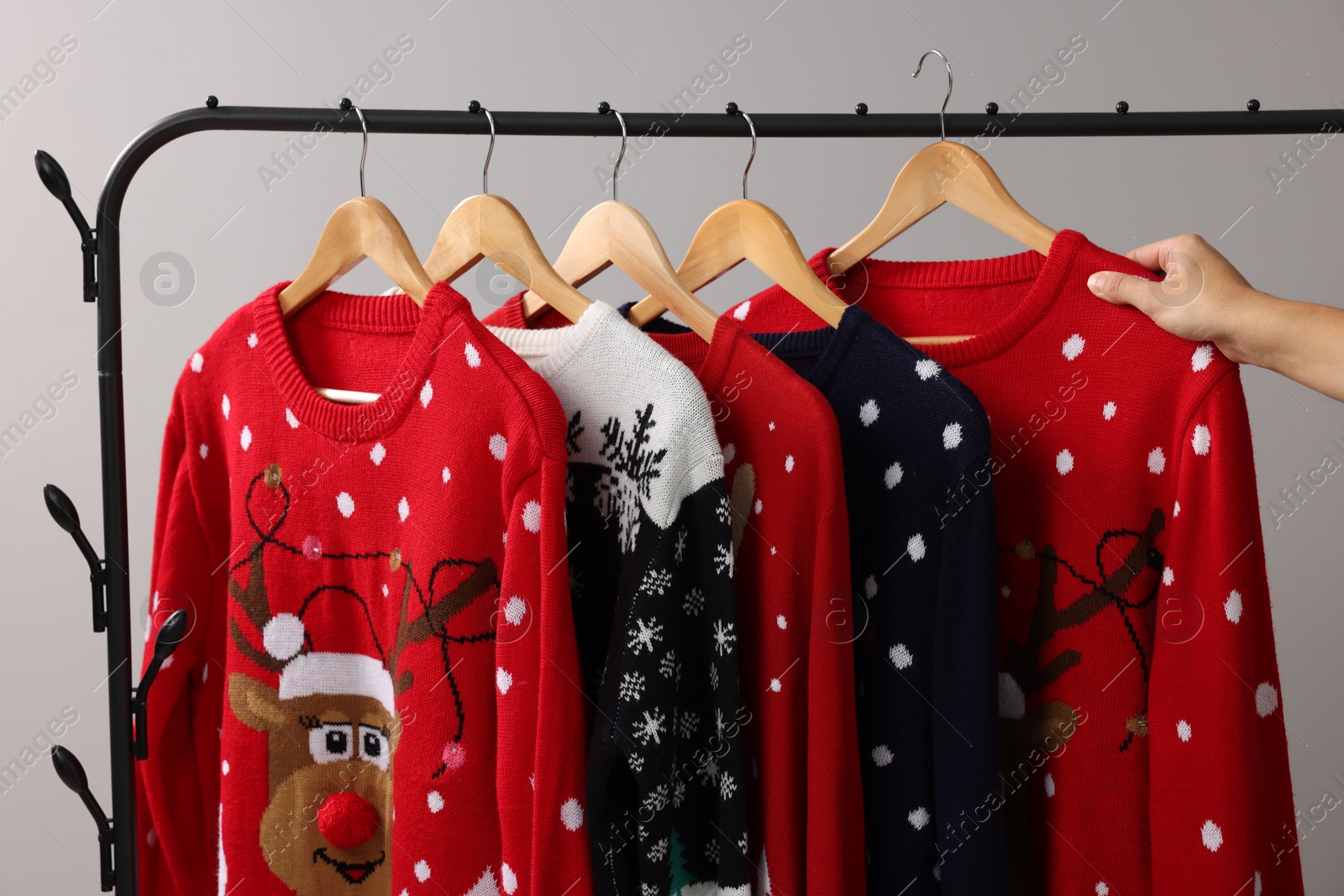 Photo of Woman picking Christmas sweater from rack near light wall, closeup