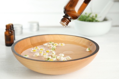 Dripping essential oil into bowl with water and flowers on table