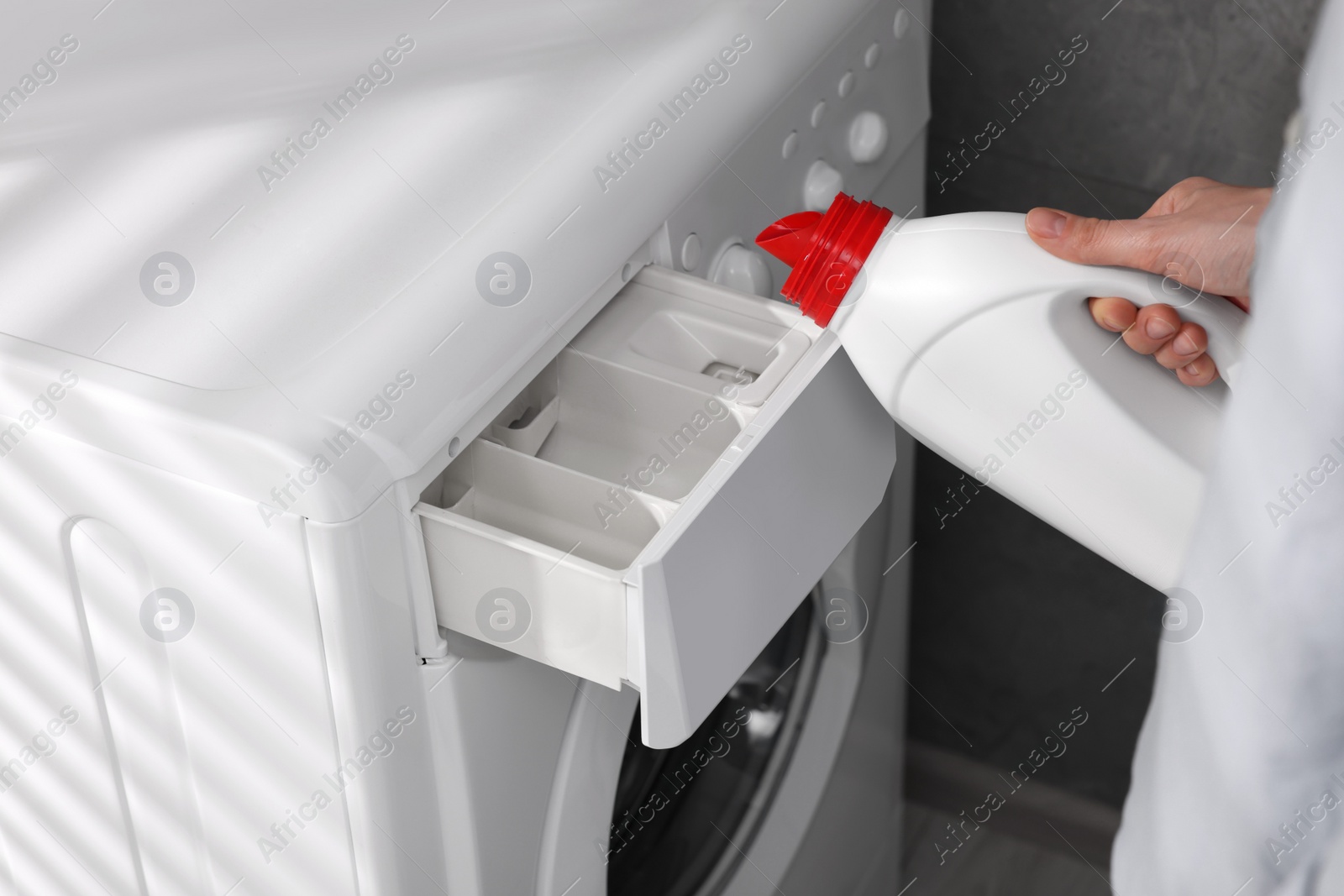 Woman pouring fabric softener from bottle into washing machine indoors, closeup Photo of Woman pouring fabric softener from bottle into washing machine indoors, closeup