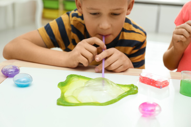 Photo of Little boy blowing slime bubble on white table indoors, closeup