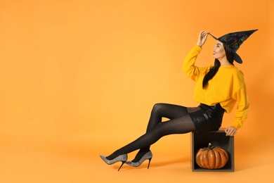 Beautiful woman wearing witch costume for Halloween party with pumpkin against yellow background, space for text