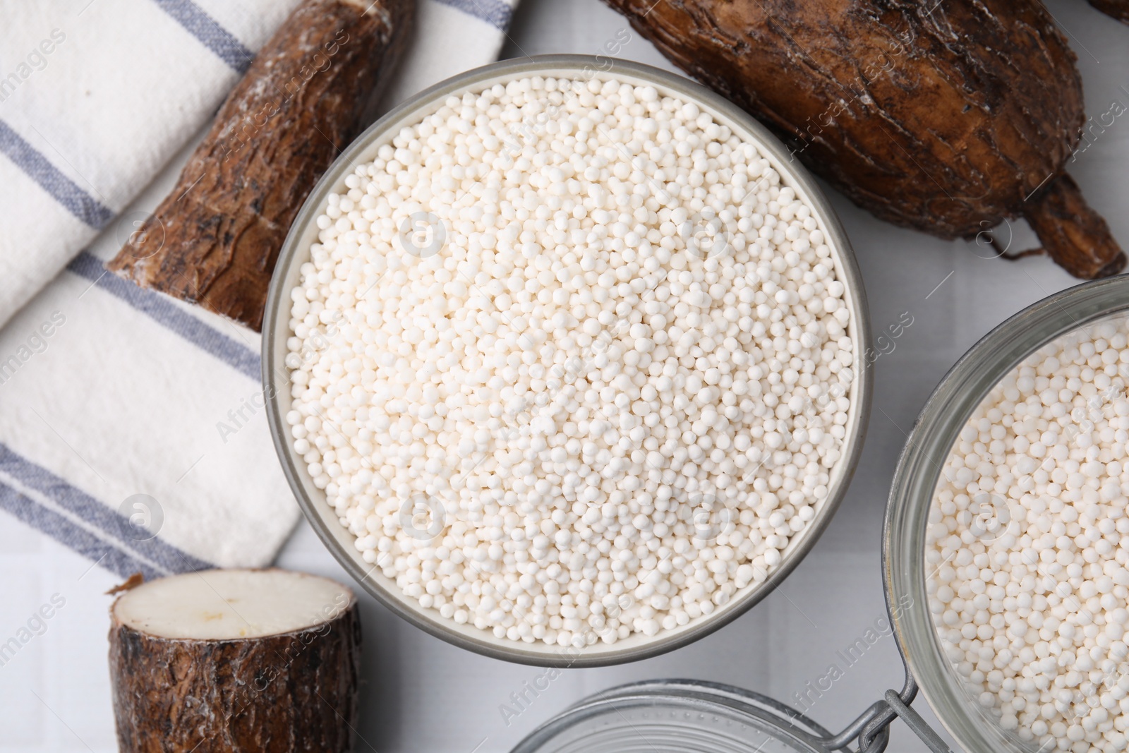 Photo of Tapioca pearls and cassava roots on white tiled table, flat lay