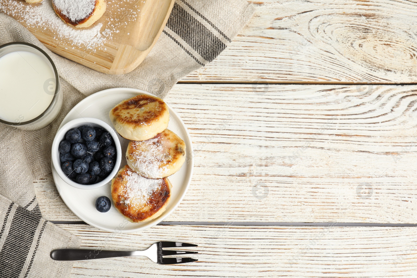 Photo of Delicious cottage cheese pancakes with blueberries and sugar powder on white wooden table, flat lay. Space for text