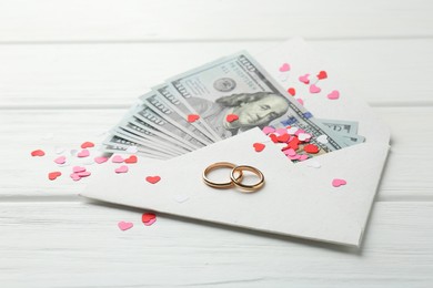 Photo of Honeymoon concept. Two golden rings, money and cutout hearts on white wooden table