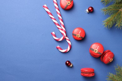 Beautifully decorated Christmas macarons, candy canes and baubles on blue background, flat lay. Space for text