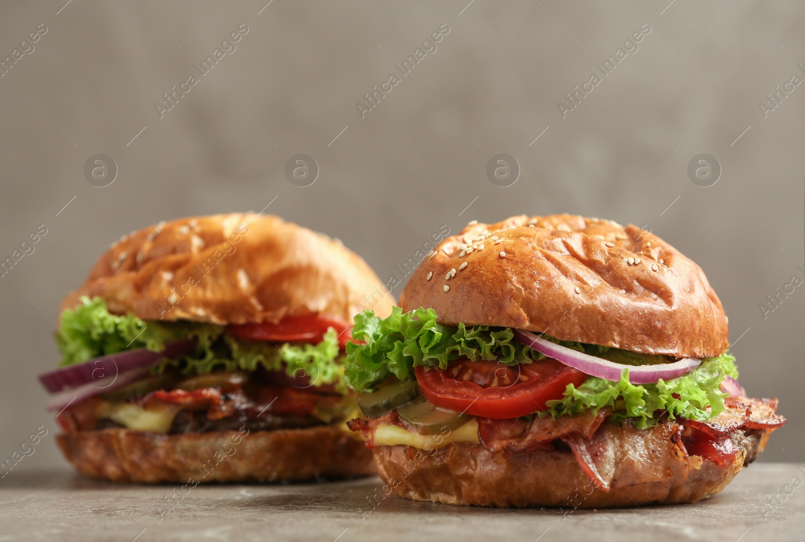 Photo of Delicious burgers with bacon on table against grey background