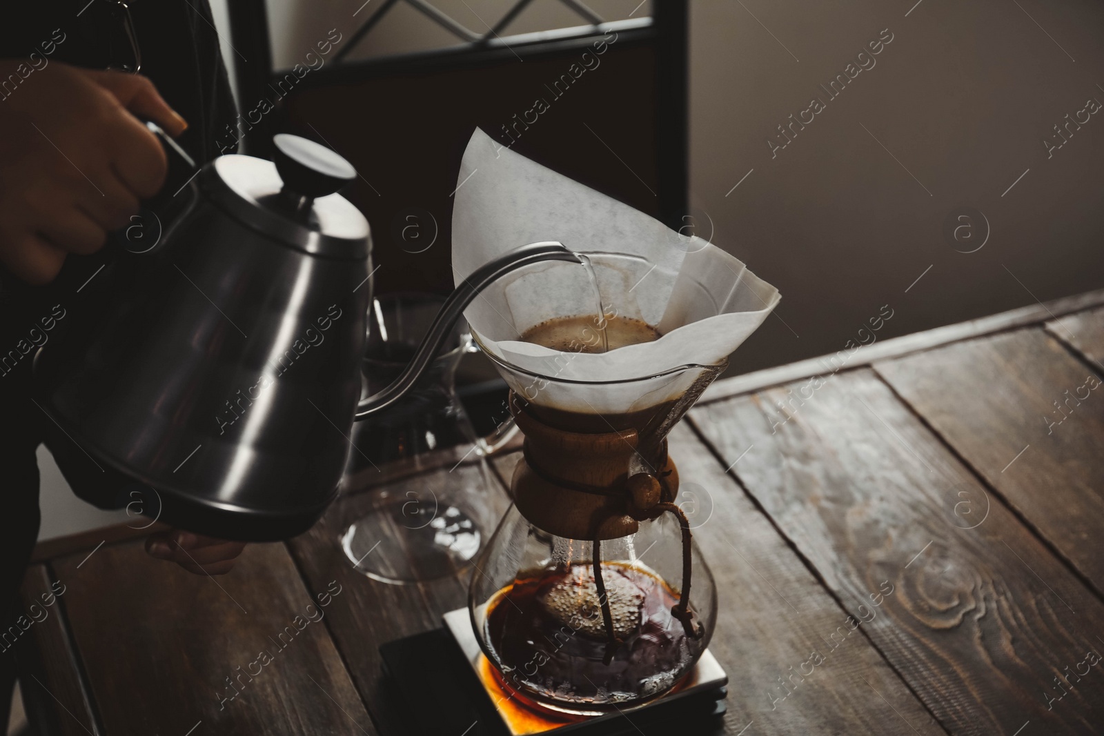 Photo of Barista pouring hot water into coffee maker at wooden table in cafe, closeup