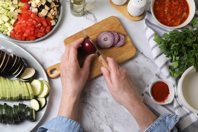 Photo of Cooking delicious ratatouille. Woman cutting fresh onion at white marble table, top view