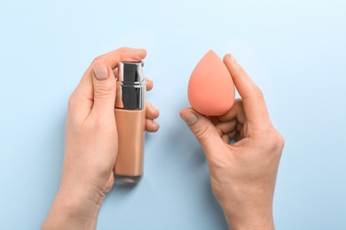Photo of Woman with makeup sponge and skin foundation on light blue background, top view
