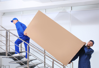 Professional workers carrying refrigerator on stairs indoors