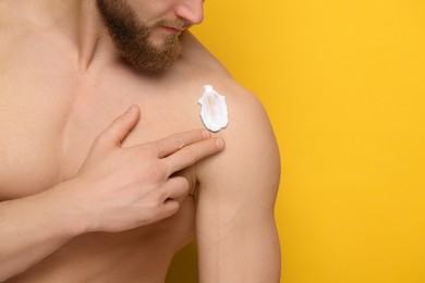 Man applying moisturizing cream onto his shoulder on orange background, closeup. Space for text