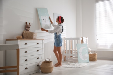 Photo of Decorator hanging picture on white wall in baby room. Interior design