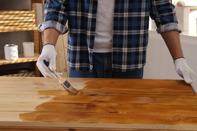 Man with brush applying wood stain onto wooden surface indoors, closeup