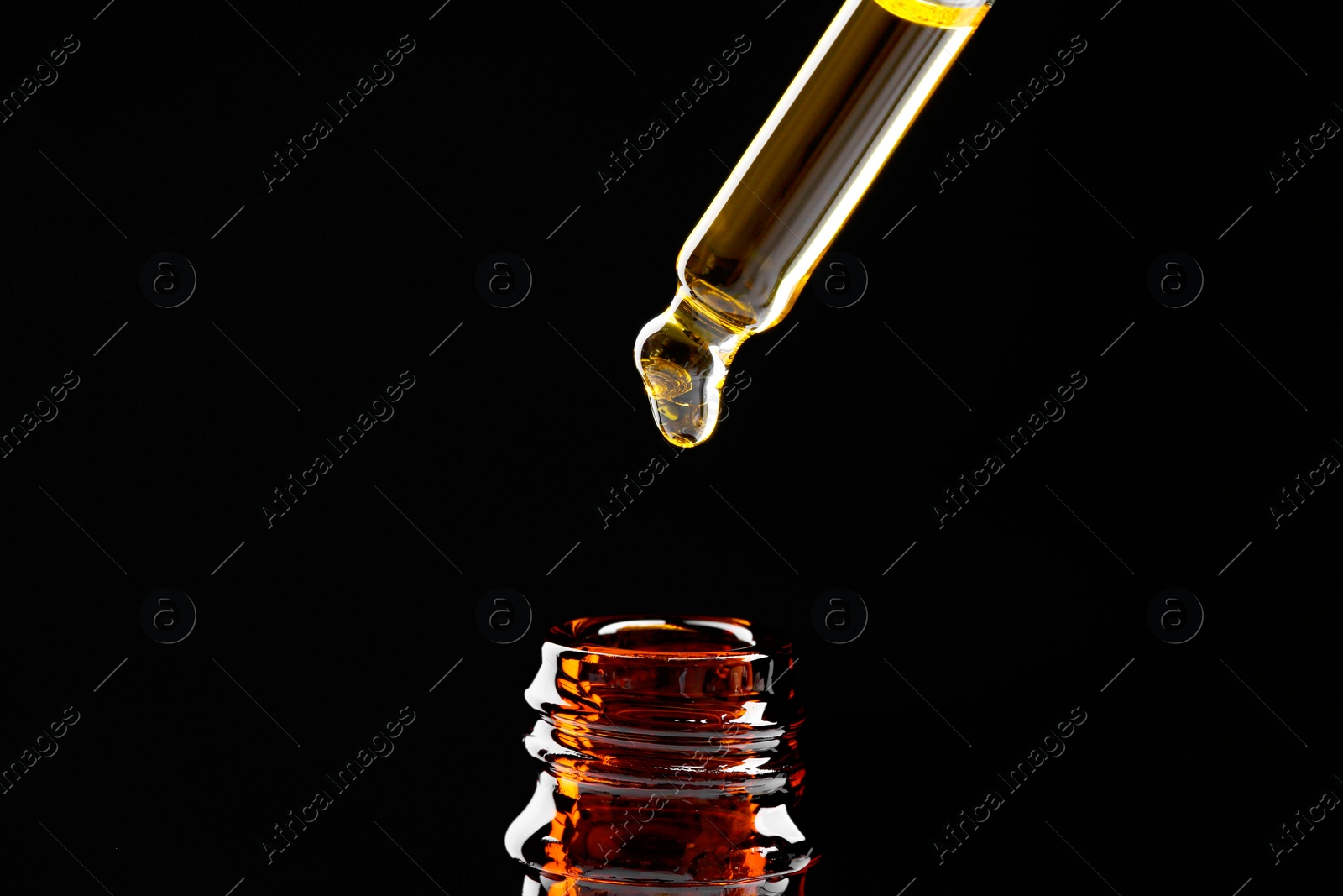 Photo of Dripping tincture from pipette into bottle on black background, closeup