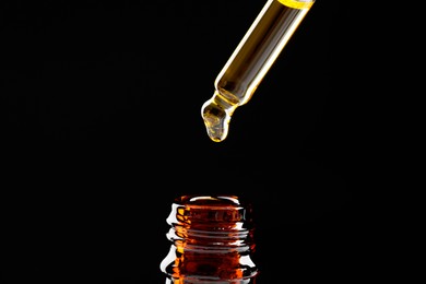 Photo of Dripping tincture from pipette into bottle on black background, closeup