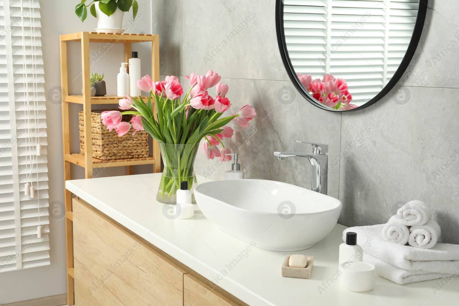 Photo of Vase with beautiful pink tulips and toiletries near sink in bathroom