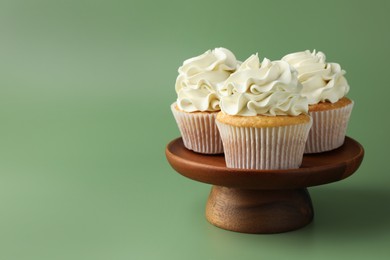 Photo of Tasty vanilla cupcakes with cream on green background, space for text