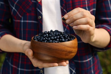 Photo of Woman putting bilberry into wooden bowl, closeup