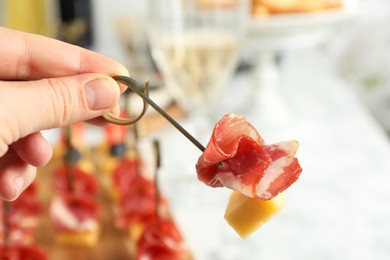 Photo of Woman holding tasty canape with cheese and prosciutto on table, closeup