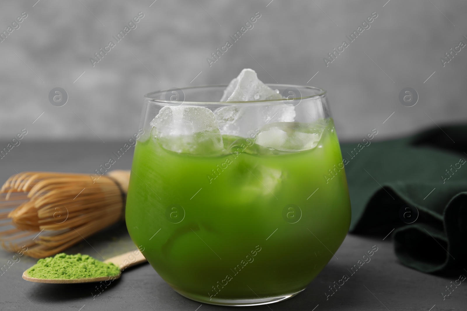 Photo of Glass of delicious iced green matcha tea, powder and bamboo whisk on grey wooden table, closeup